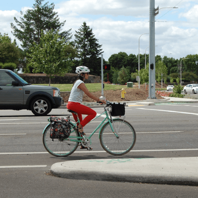 A cyclist prepared to cross an intersection. There is a truck in the lane next to them.